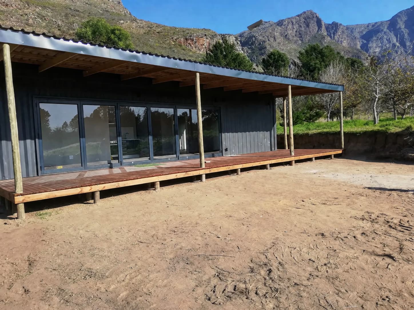Johannes' container home under a covered wooden deck, set against a mountain backdrop